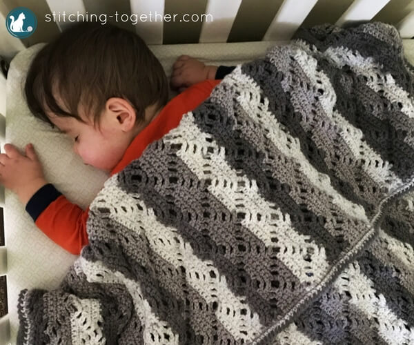 baby sleeping under gray and white diamond lace crochet baby blanket