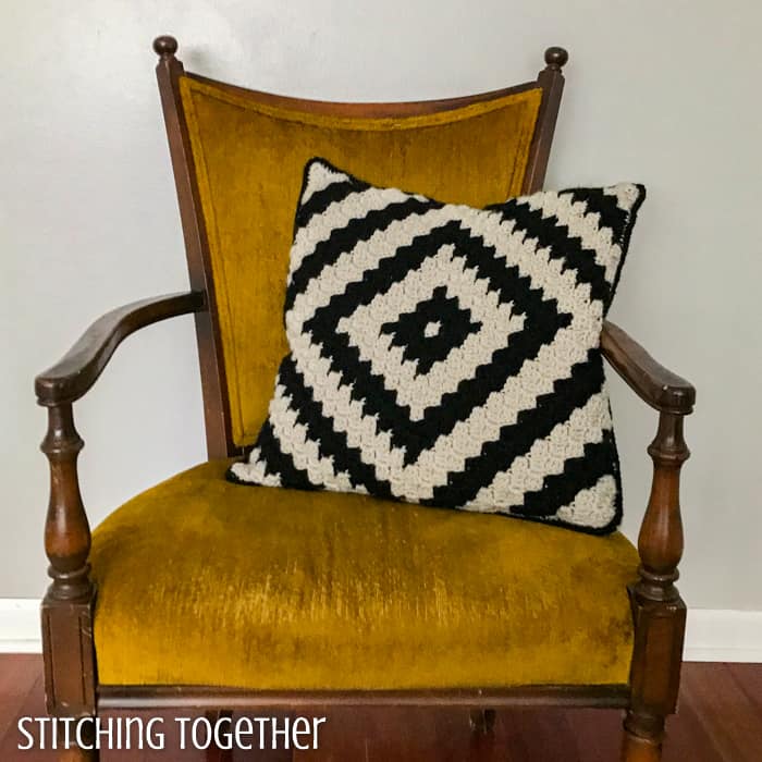 modern crochet pillow in black and ivory still on a yellow chair