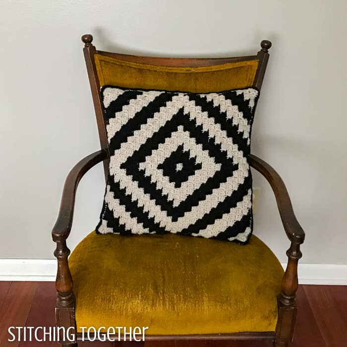 geometric crochet pillow in black and ivory still on a yellow chair