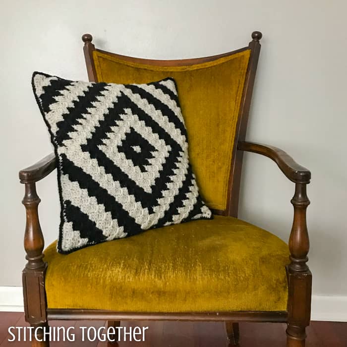 modern crochet pillow in black and ivory still on a yellow chair