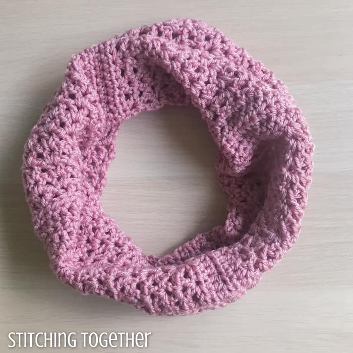 pink crochet cowl with open stitches sitting on a surface