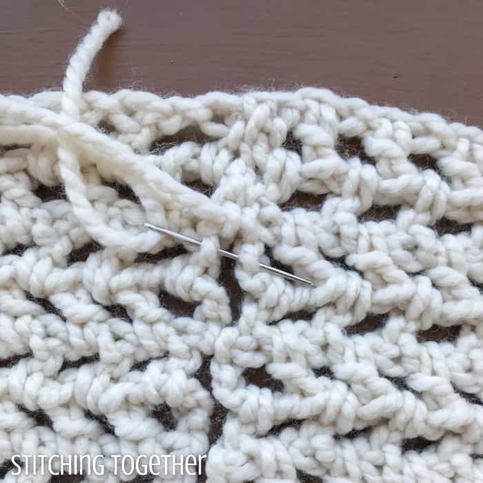 close up of yarn and needle being used to join crochet fabric