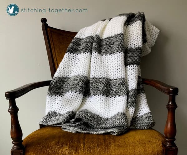 gray and white v stitch crochet blanket draped on yellow chair