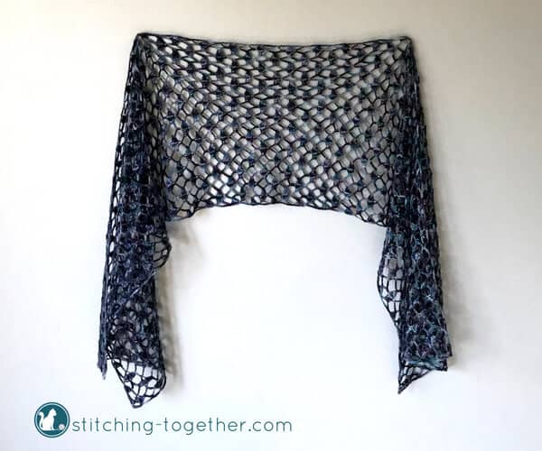 lacy crochet scarf with open shell stitches hanging on a wall