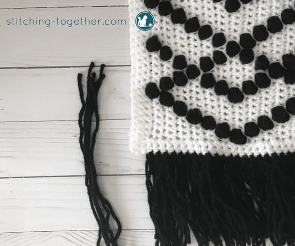 white crochet fabric with black puff stitches and fringe 