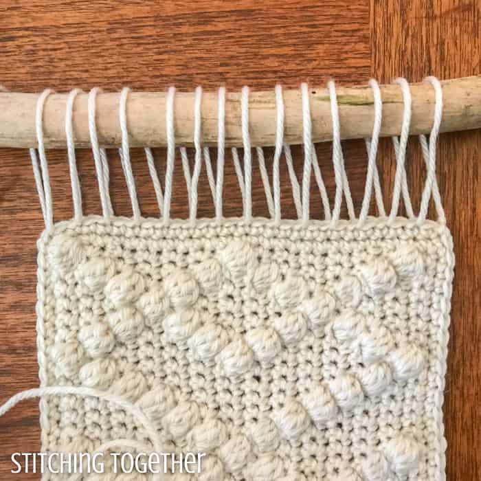 wall hanging being attached with yarn to a wooden stick