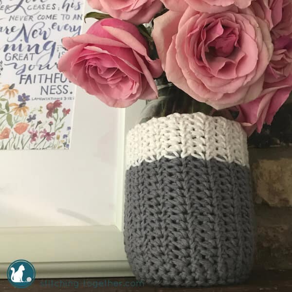 gray and white crochet mason jar cozy holding pink roses