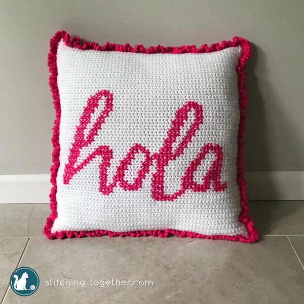 white crochet pillow with word hola crossed stitched