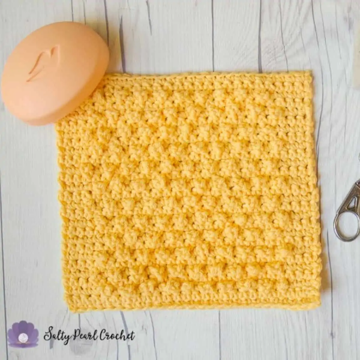 yellow crochet dishcloth laying flat with a bar of soap on top