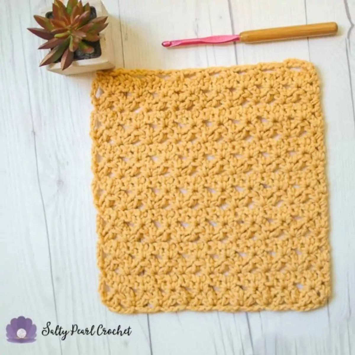 yellow crochet washcloth laying flat next to a plant and a crochet hook