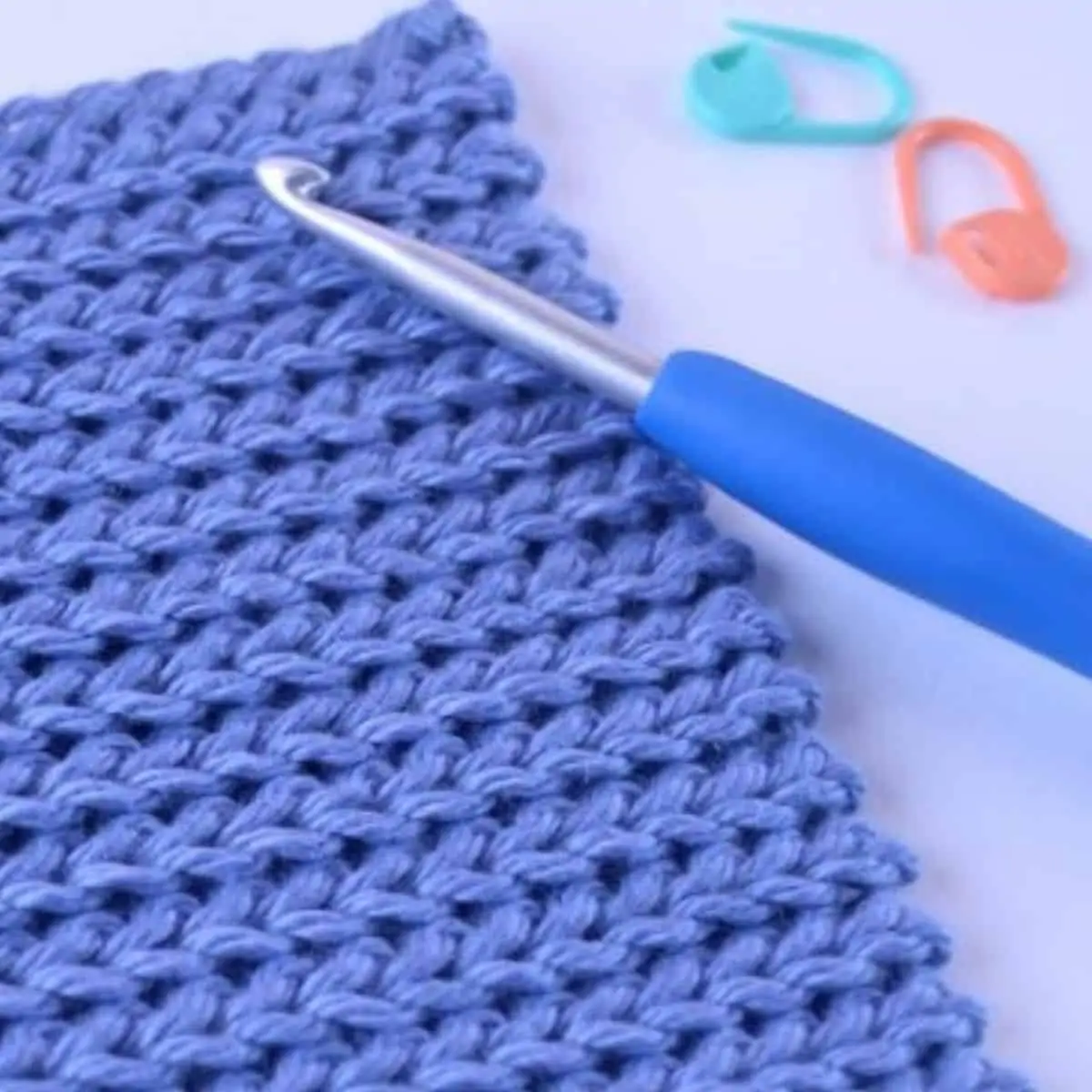 close up of a purple ribbed crochet fabric with hook and stitch markers