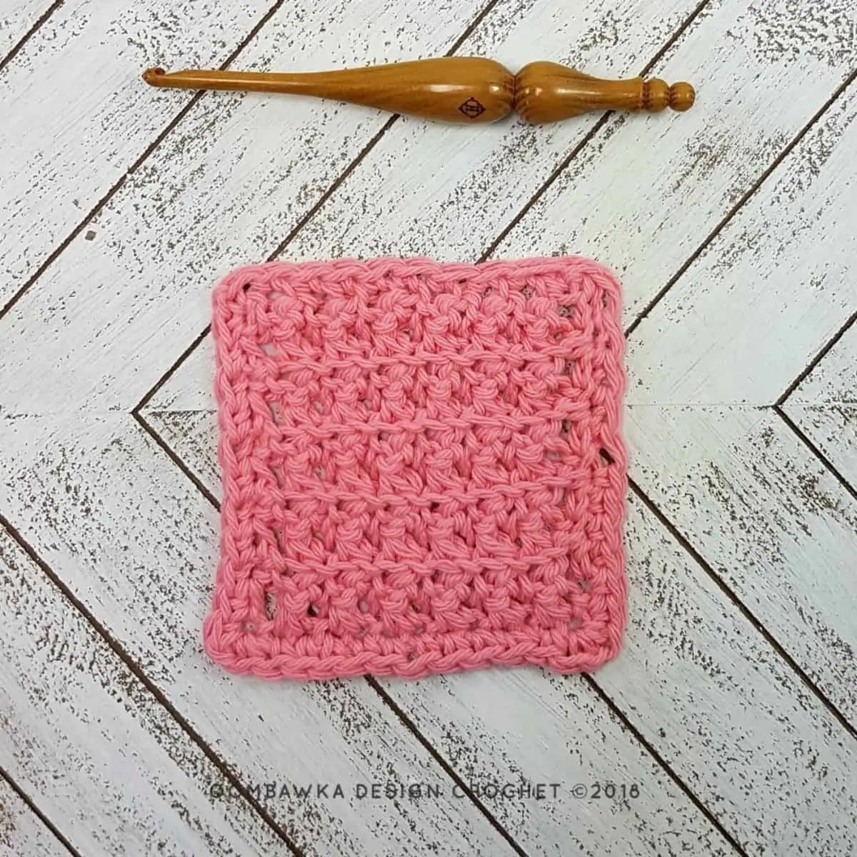 small pink square crochet stitches swatch laying flat next to a wooden crochet hook