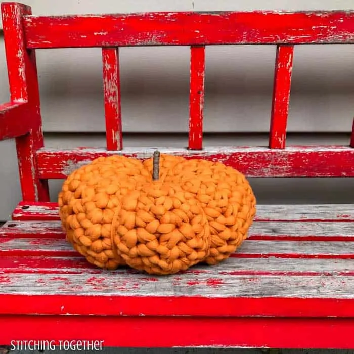 large crochet pumpkin sitting on a red bench 