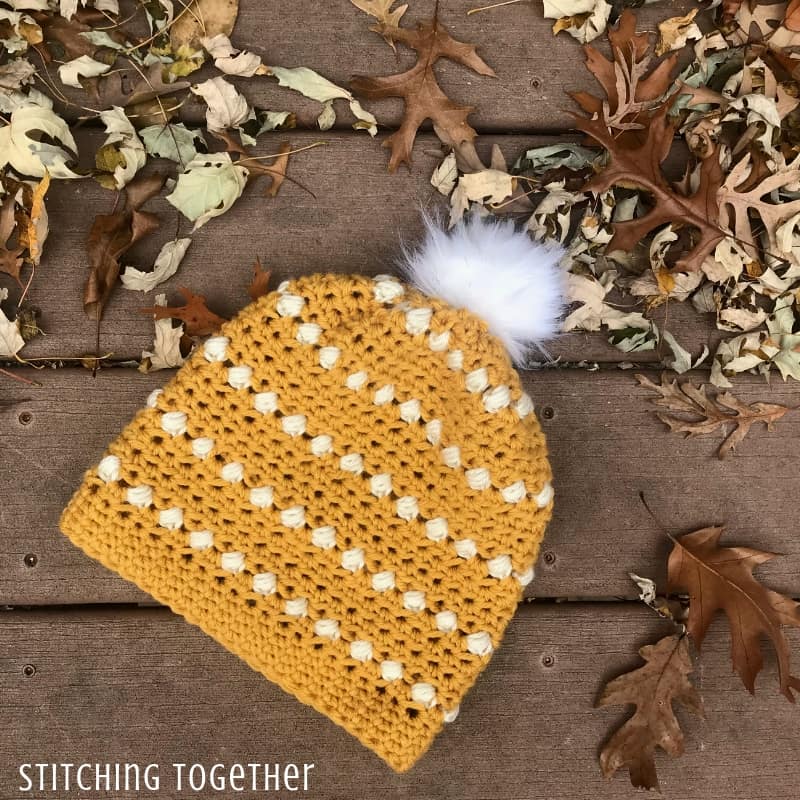 Mustard colored puff stitch crochet hat on ground surrounded by leaves