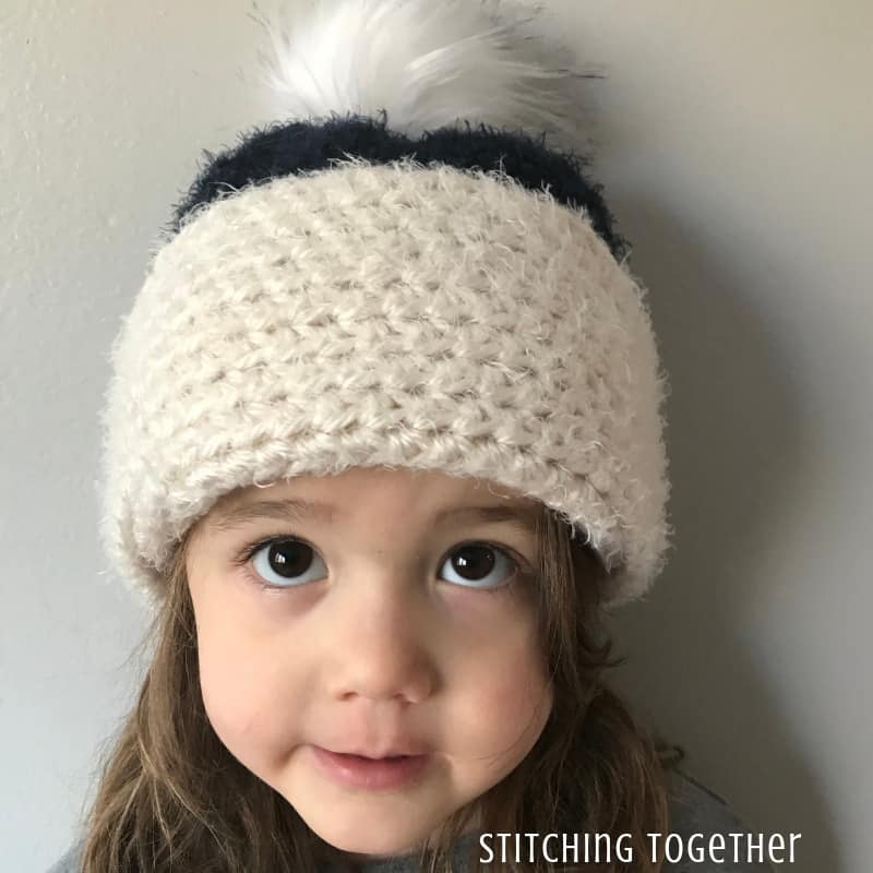 child with big brown eyes wearing a half double crochet hat