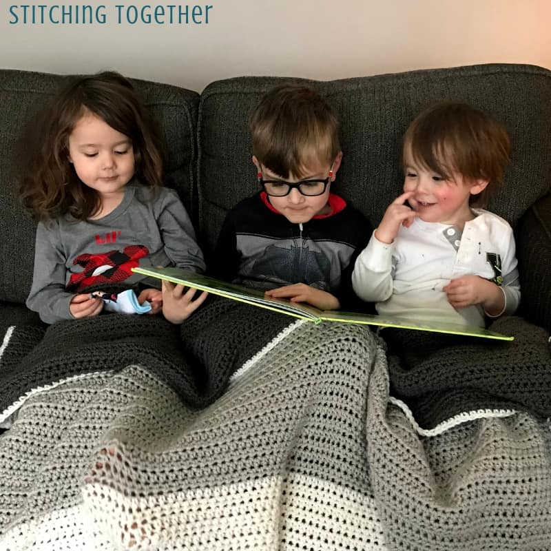 3 kids reading on a couch covered in a crochet blanket