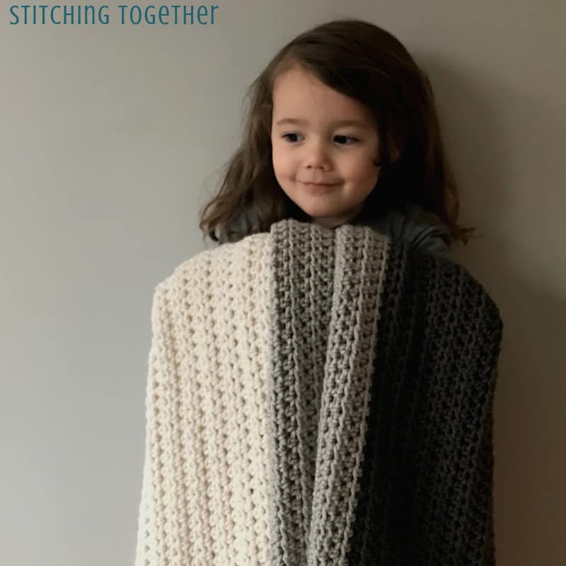 young girl holding gray striped half double crochet afghan