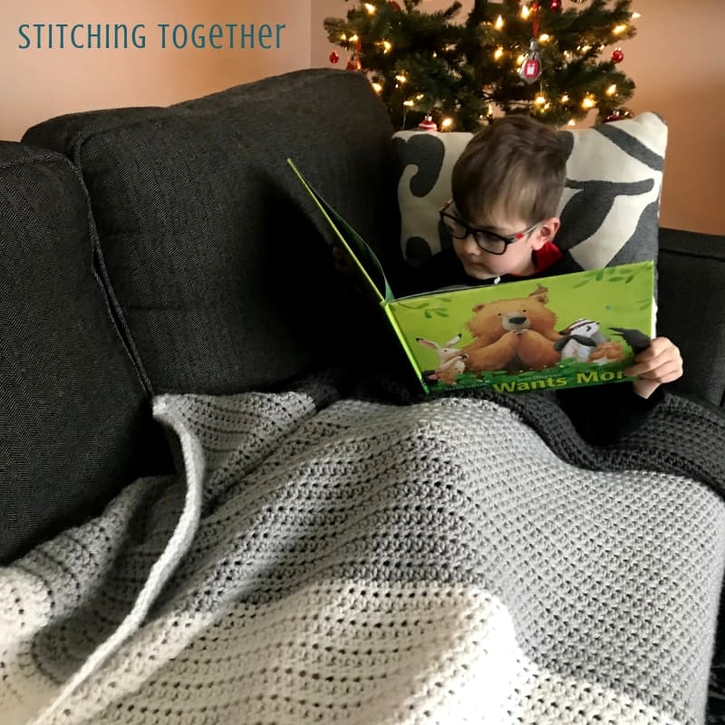 Boy reading on couch covered in a gray striped hdc blanket