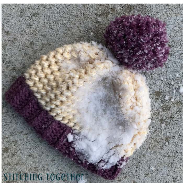 chunky crochet hat with pom pom and snow on it