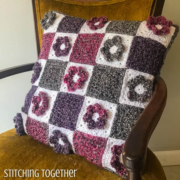 granny square crochet flower pillow sitting on a chair