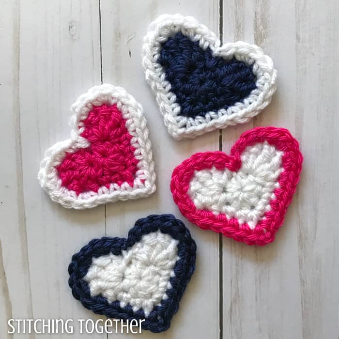 pink, white and blue crochet hearts laying on a wood background