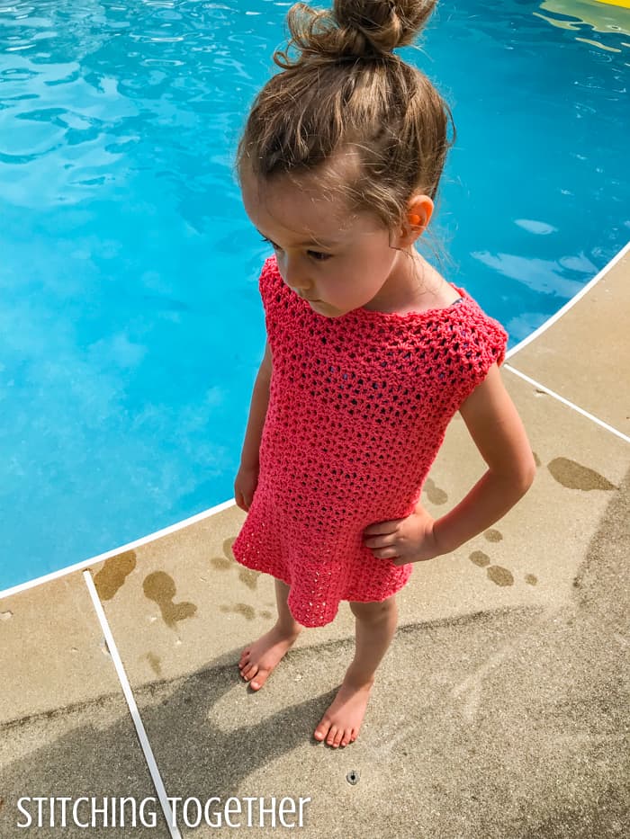 top view of a little girl in a pink crochet dress standing by a pool