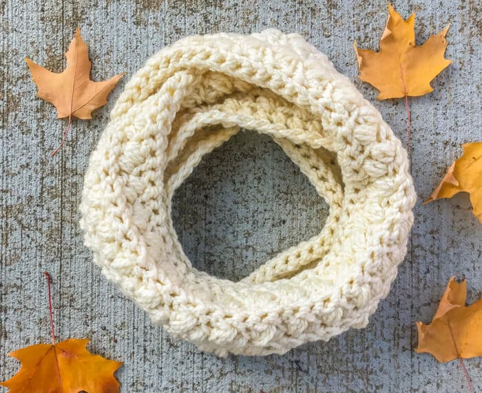chunky crochet infinity scarf looped on the ground and surrounded by fall leaves