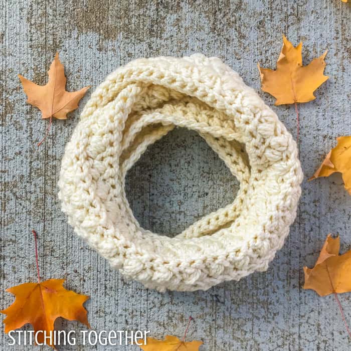 chunky crochet infinity scarf looped on the ground and surrounded by fall leaves