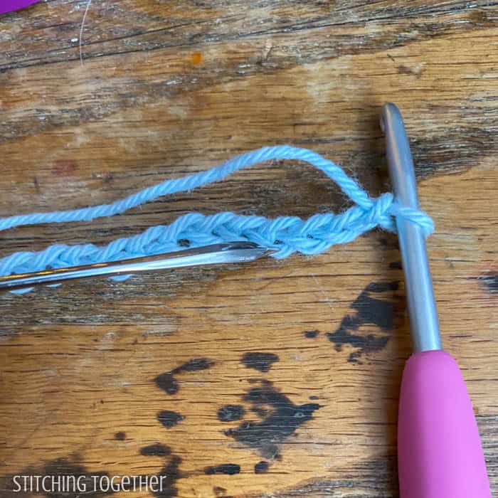 crochet chain on a hook with a needle pointing to the bottom loop