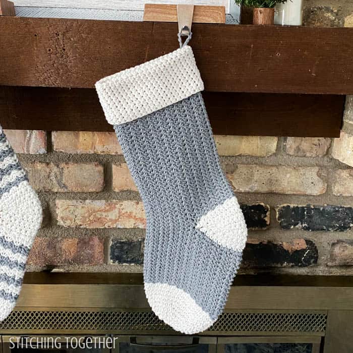 gray and white crochet christmas stocking hanging on a mantle