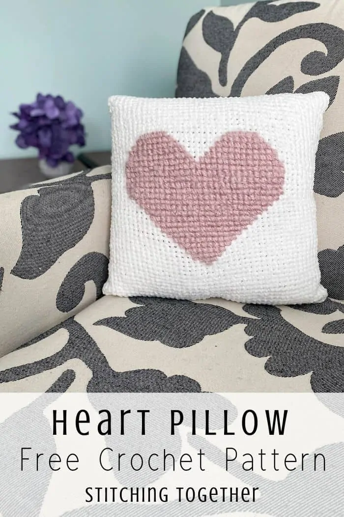 White crochet pillow with pink heart sitting on a chair