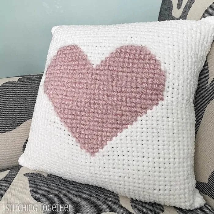 white and pink heart crochet pillow sitting on a chair
