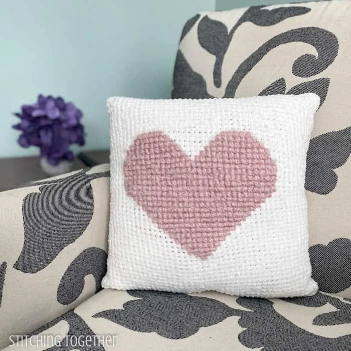 White crochet heart pillow sitting on a chair