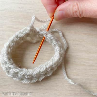 orange yarn needle working yarn through a stitch