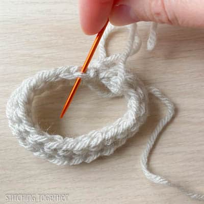 orange yarn needle working yarn through a stitch