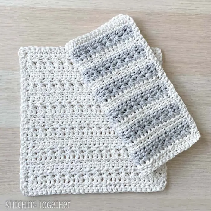 2 crochet dishcloths one folded and with striped laying on top of a cream dishcloth