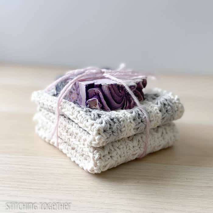 two crochet washcloths folded and stacked with a bar of soap on the top