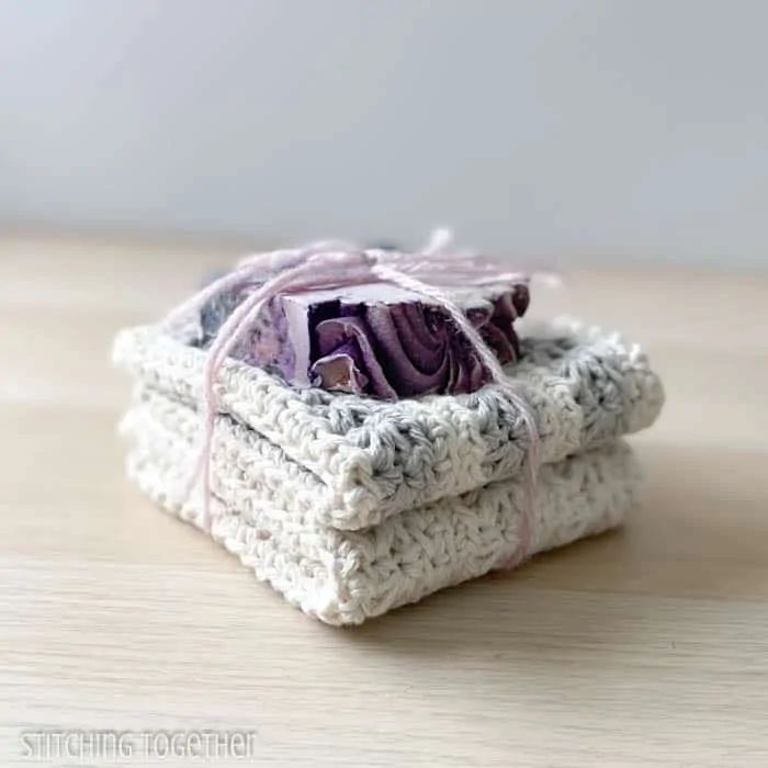 two crochet washcloths folded and stacked with a bar of soap on the top