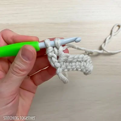 left hand holding yarn and a crochet hook showing the steps of a stitch