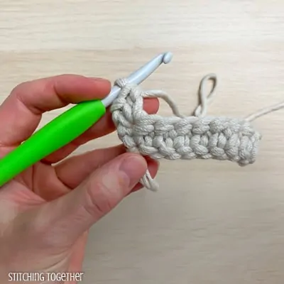 left hand holding yarn and a crochet hook showing the steps of a stitch