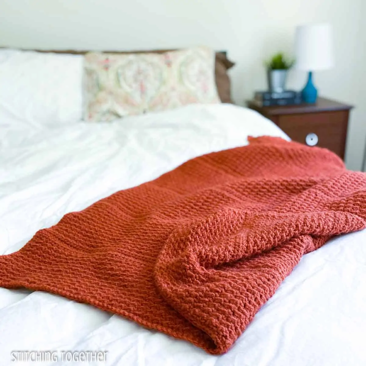 terracotta crochet lap throw draped on a bed