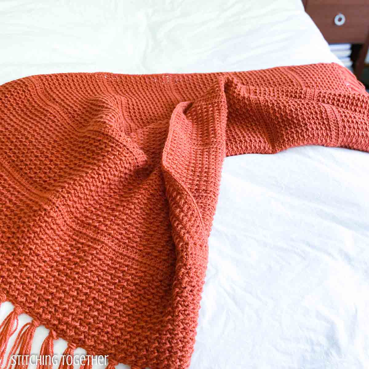 orange crochet throw blanket draped on a bed