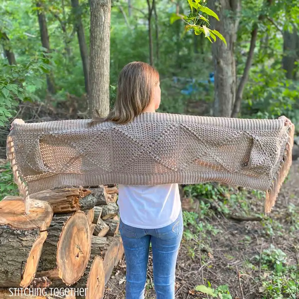 woman holding out a crochet shawl with pockets