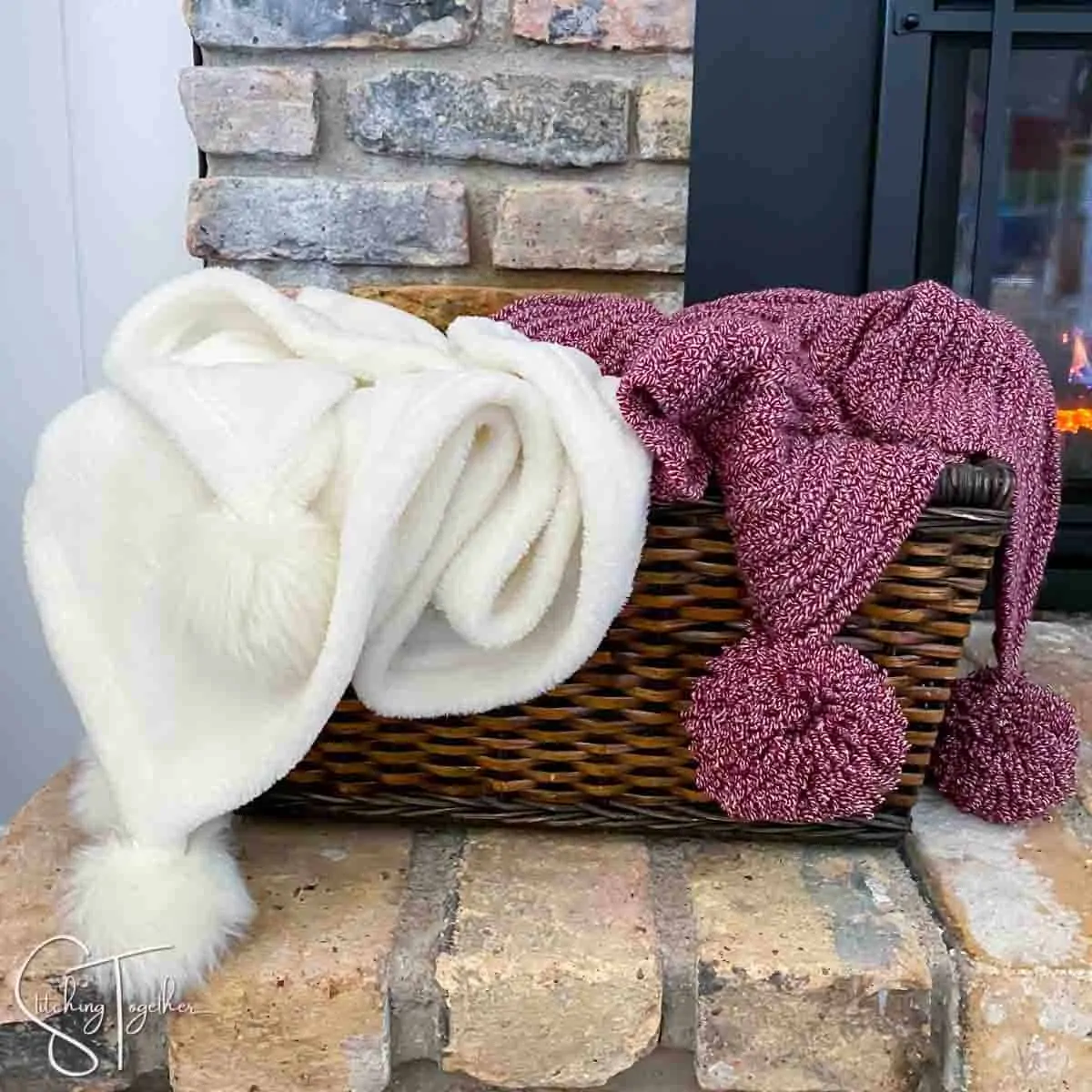 a white blanket and a red crochet christmas blanket both with pom poms in a basket