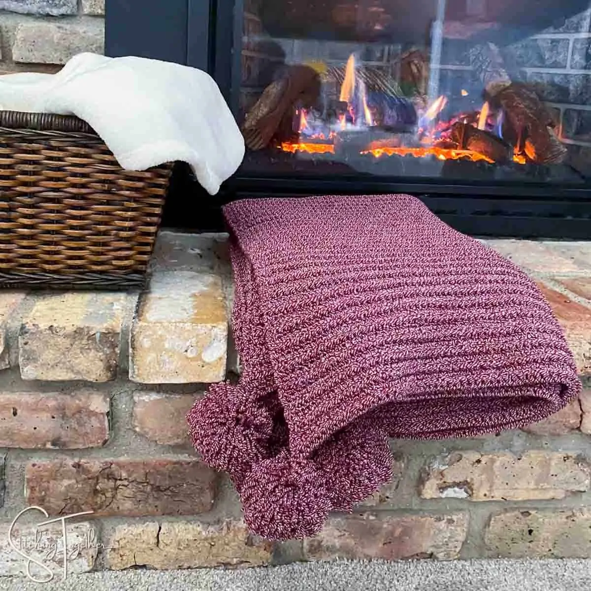 red crochet blanket with pom poms folded on the hearth of a fireplace