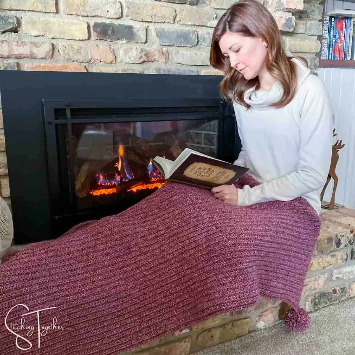 lady covered in a simple crochet christmas blanket while reading in front of a fireplace