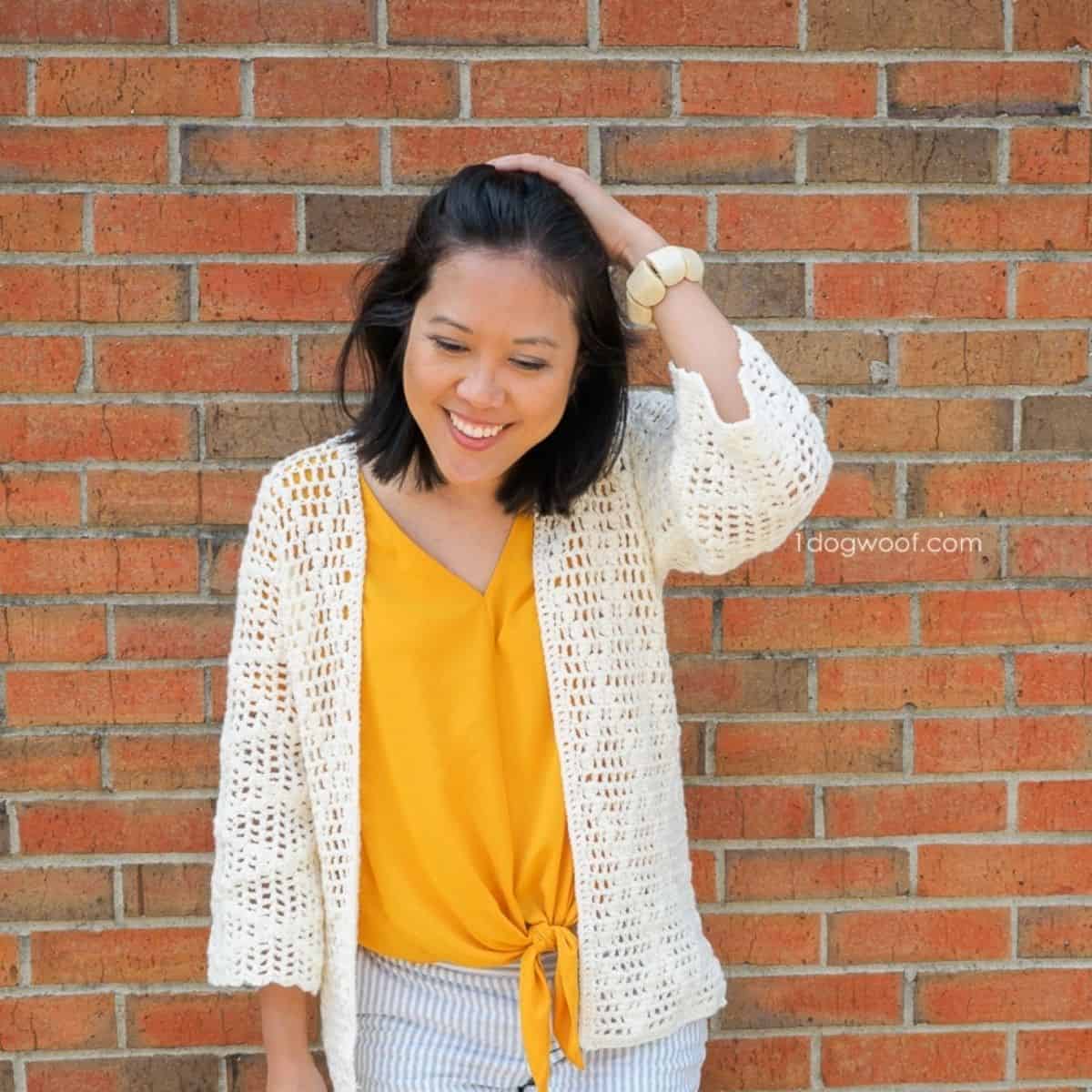 woman wearing a thin yarn cardigan in front of a brick wall