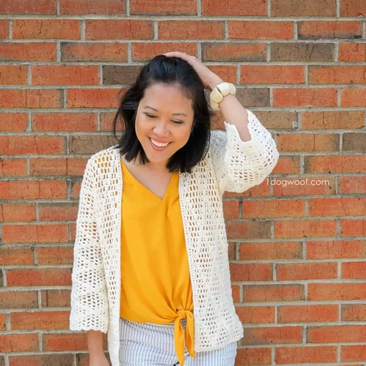 woman wearing a thin yarn cardigan in front of a brick wall