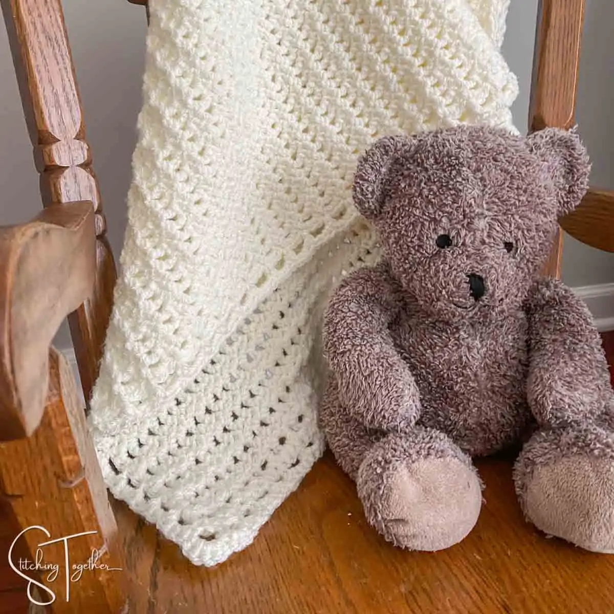 lacy crochet baby blanket draped on chair with stuffed bear next to it