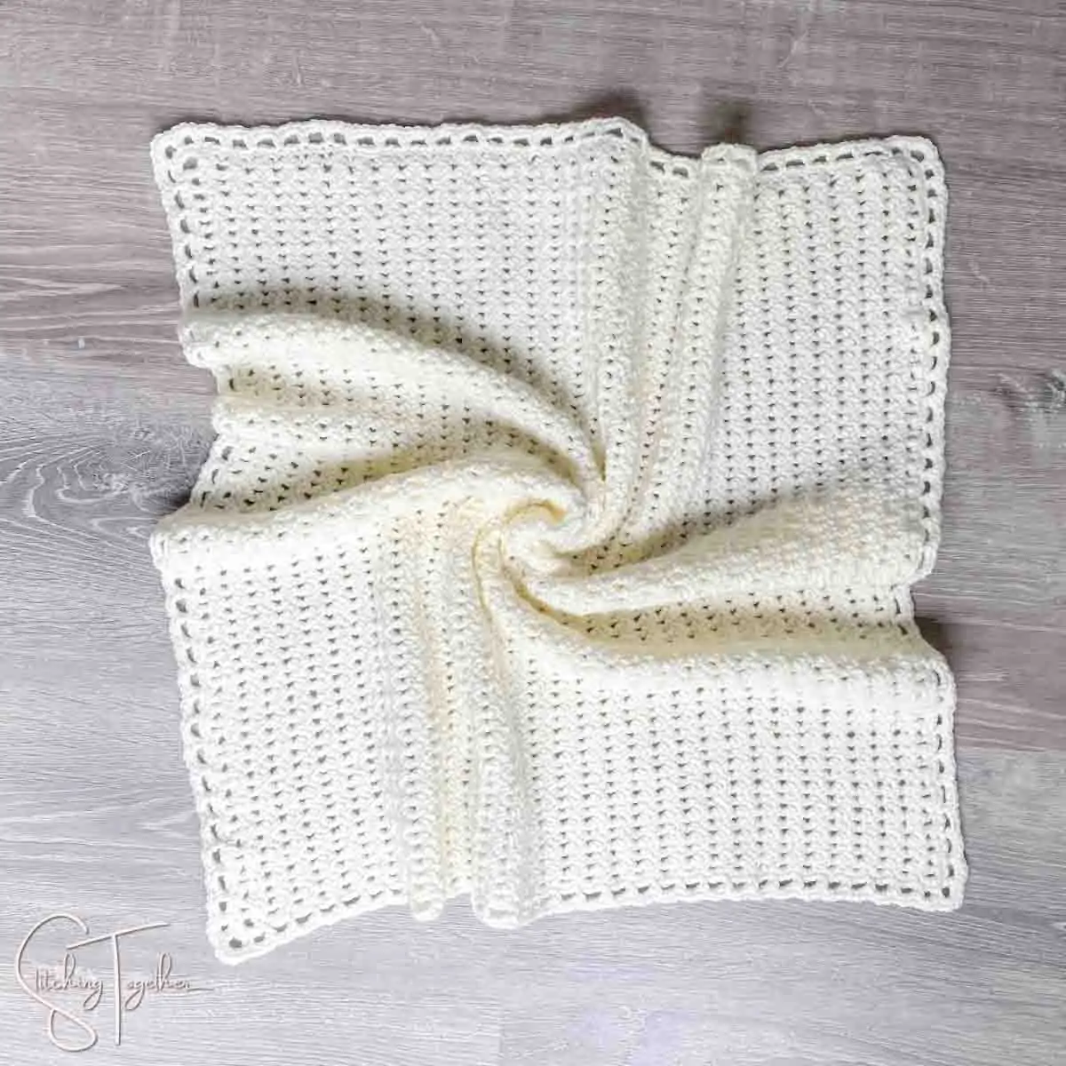 neutral crochet baby blanket laid out on the floor